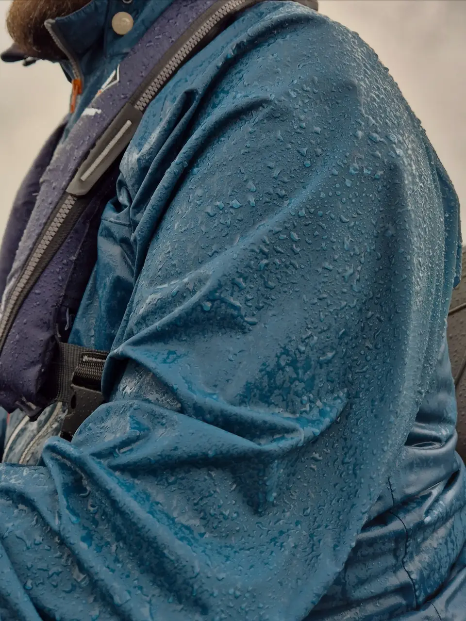Rękaw kurtki wędkarskiej z membraną pokryty kroplami deszczu, na kurtce kamizelka asekuracyjna